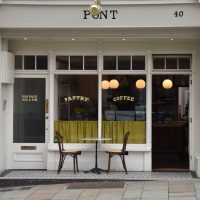 The front of Pont as seen from the south side of Wyle Cop in Shrewsbury. The open door is on the right with two windows to the left, while in front of those, on the recessed, tiled threshold, is a classic two-person round table, Pont's only seating.