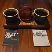 Two filter coffees, one either side of a glass of cold brew, all served on a small tray along with two information cards for the coffees.